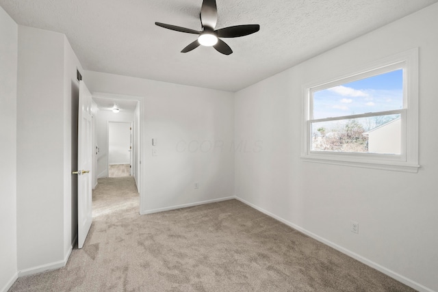 spare room with a ceiling fan, baseboards, a textured ceiling, and light colored carpet