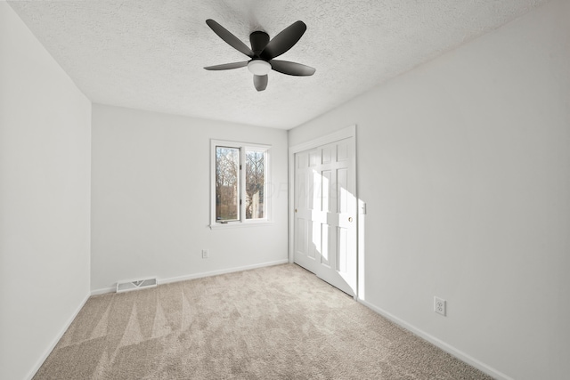 unfurnished bedroom featuring a textured ceiling, light colored carpet, visible vents, baseboards, and a closet