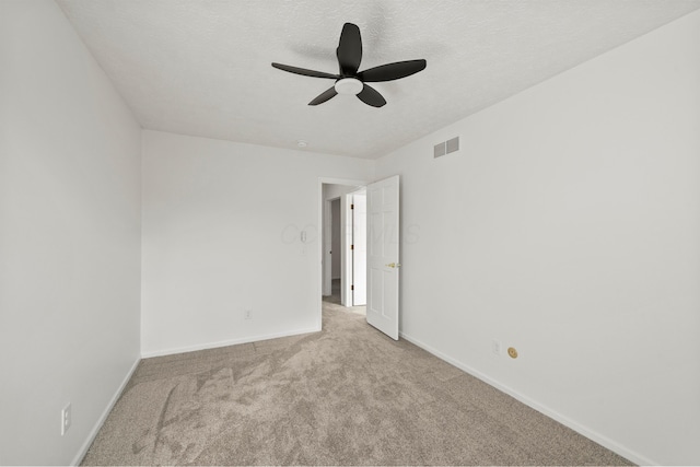 spare room with ceiling fan, a textured ceiling, light carpet, visible vents, and baseboards