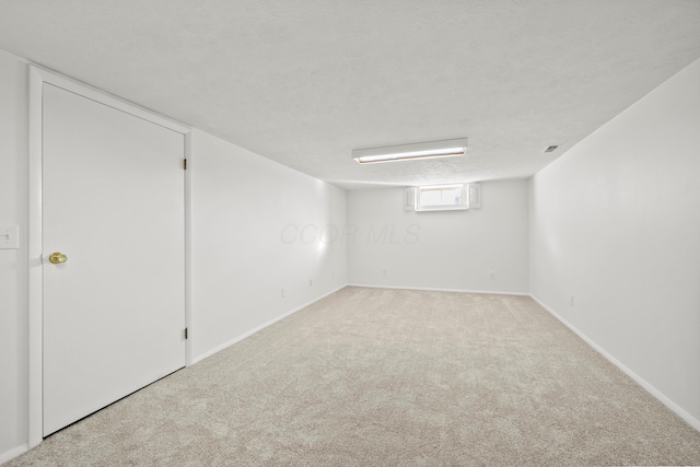 basement featuring light carpet, a textured ceiling, and baseboards