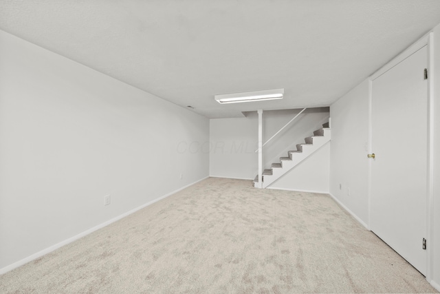 finished below grade area featuring stairs, baseboards, and light colored carpet