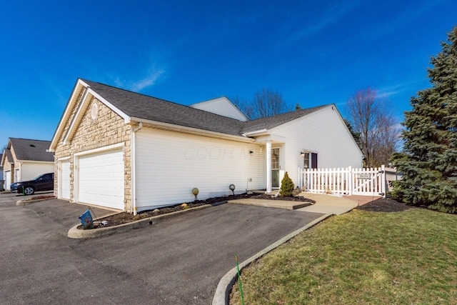 view of side of property with driveway, a lawn, stone siding, an attached garage, and fence