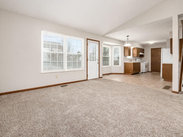 unfurnished living room with lofted ceiling, baseboards, visible vents, and light colored carpet