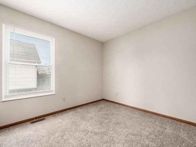 empty room featuring light colored carpet, visible vents, a textured ceiling, and baseboards