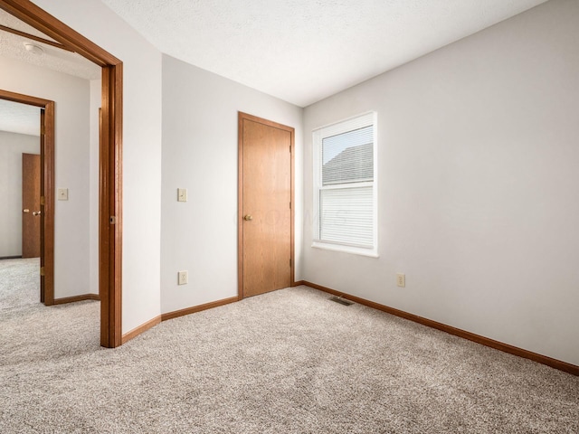 unfurnished bedroom featuring carpet, visible vents, a textured ceiling, and baseboards