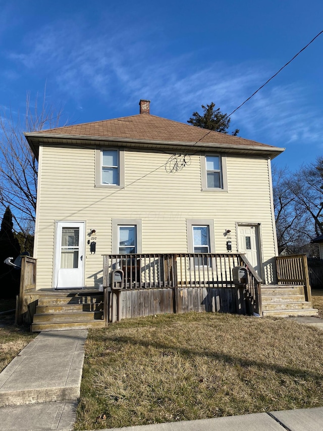 back of house featuring a chimney, a wooden deck, and a lawn