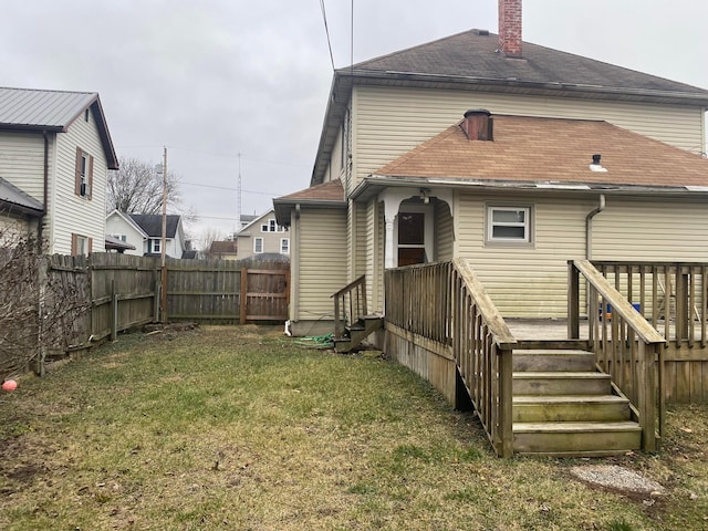 rear view of house with entry steps, a fenced backyard, a shingled roof, a yard, and a chimney