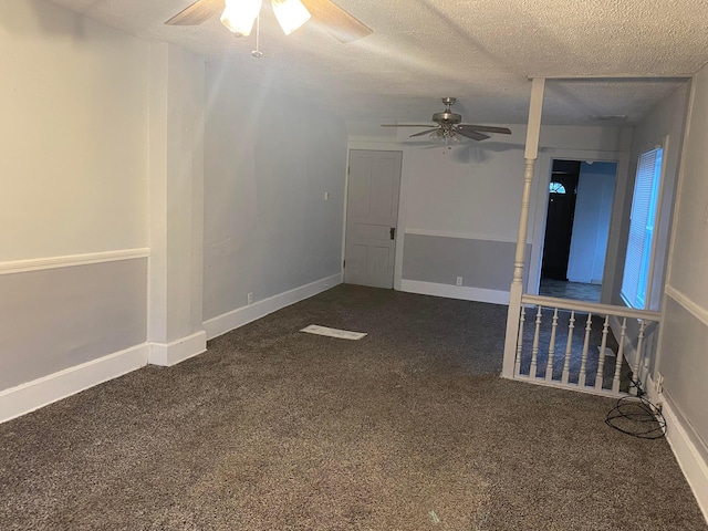 empty room featuring a textured ceiling, dark colored carpet, a ceiling fan, and baseboards