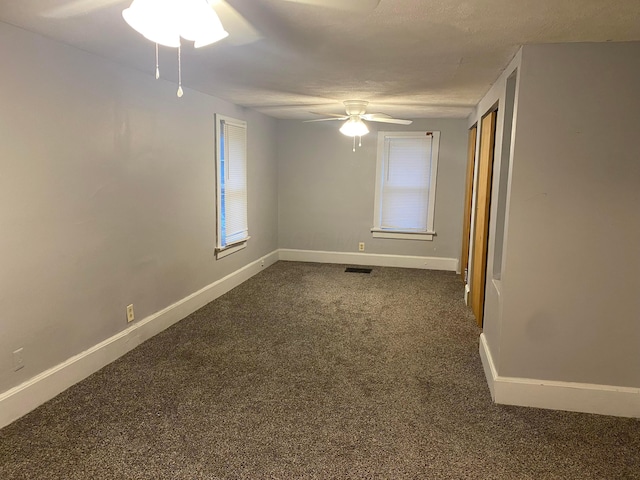 unfurnished room featuring visible vents, dark carpet, ceiling fan, and baseboards