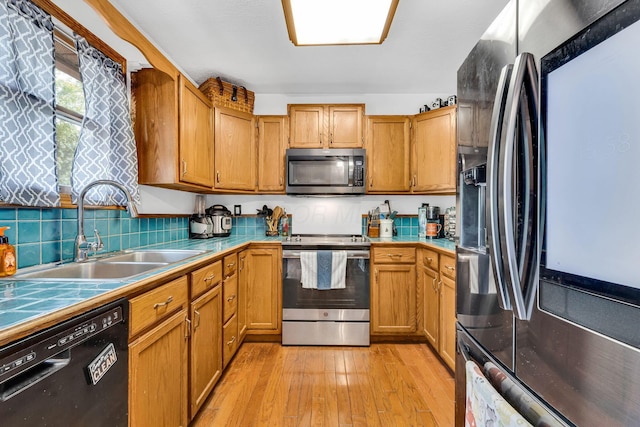 kitchen with a sink, backsplash, tile countertops, stainless steel appliances, and light wood-style floors