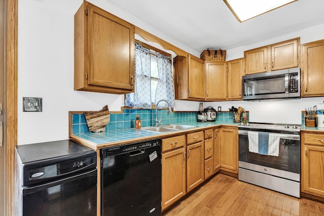 kitchen with tile counters, light wood finished floors, appliances with stainless steel finishes, and a sink