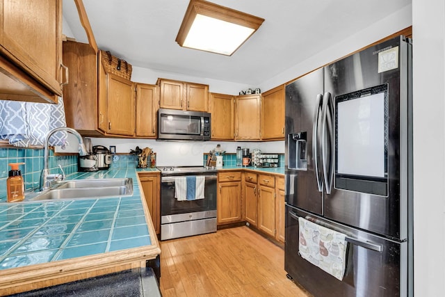 kitchen with light wood-style flooring, a sink, backsplash, stainless steel appliances, and tile counters