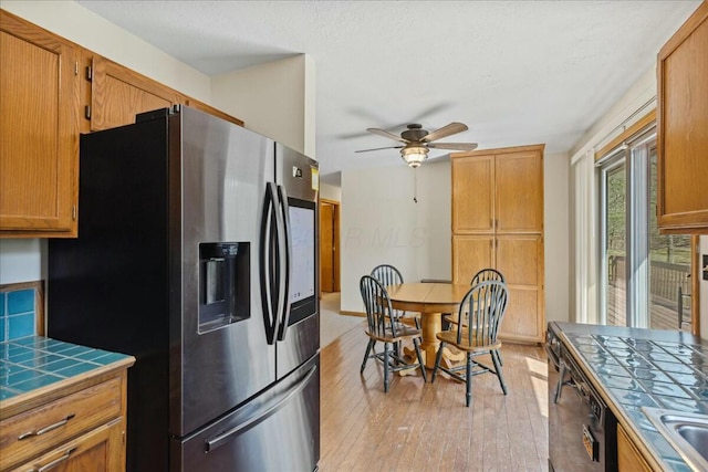 14580 Monroe Mills Rd, Mount Vernon, OH 43050 - kitchen featuring tile counters, light wood finished floors, dishwasher, a ceiling fan, and stainless steel refrigerator with ice dispenser