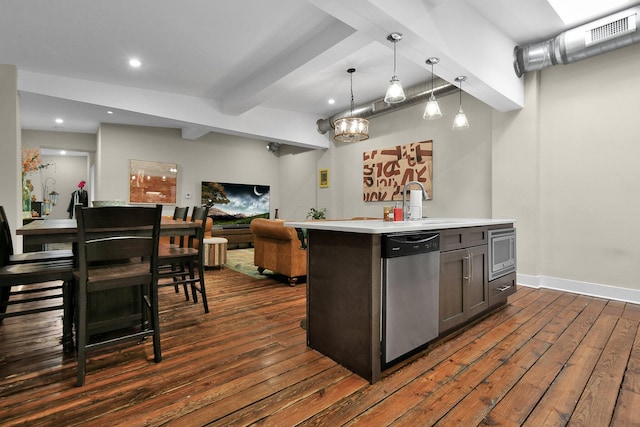 kitchen featuring dark wood-style floors, beam ceiling, light countertops, appliances with stainless steel finishes, and a kitchen island with sink