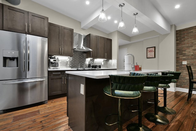 kitchen featuring dark wood-style floors, beam ceiling, stainless steel refrigerator with ice dispenser, backsplash, and wall chimney range hood