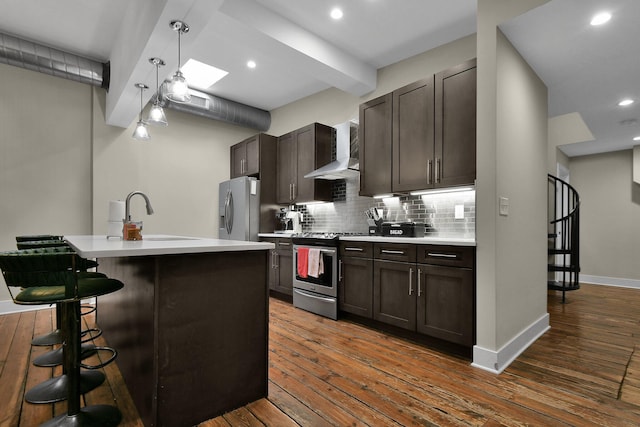 kitchen featuring wall chimney exhaust hood, a kitchen breakfast bar, light countertops, stainless steel appliances, and a sink