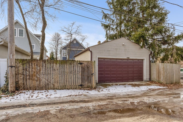 snow covered garage featuring a detached garage and fence