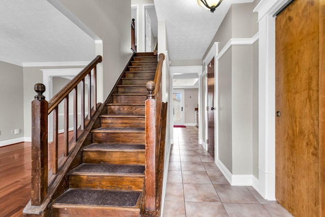 staircase featuring a textured ceiling, ornamental molding, tile patterned flooring, and baseboards