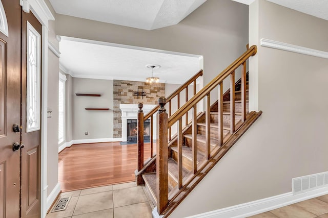 foyer entrance with light tile patterned floors, visible vents, baseboards, a fireplace with flush hearth, and stairway