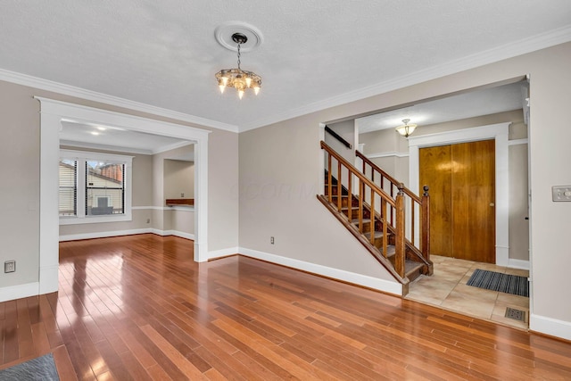 spare room with baseboards, ornamental molding, wood finished floors, stairs, and a notable chandelier