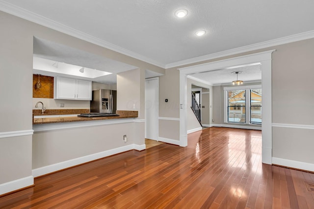 unfurnished living room featuring crown molding, a textured ceiling, baseboards, and wood finished floors