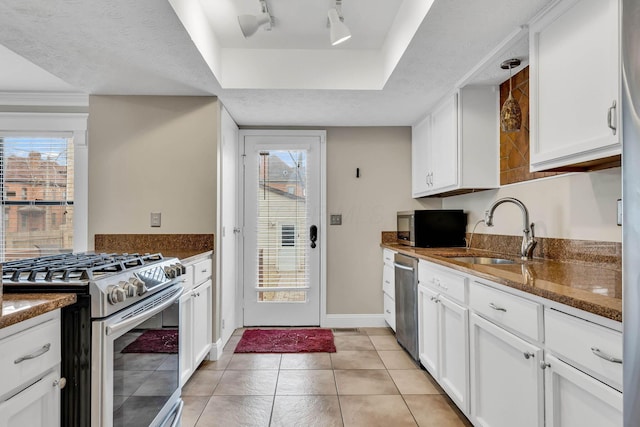 kitchen featuring white cabinets, dark stone countertops, stainless steel appliances, and a sink