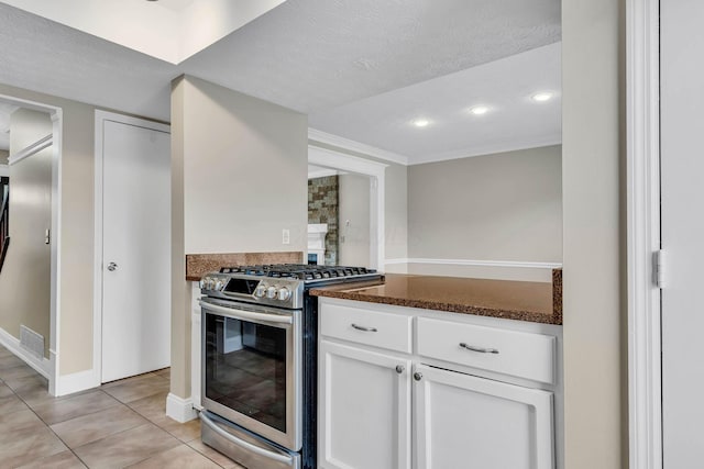 kitchen with light tile patterned floors, stainless steel gas range oven, visible vents, ornamental molding, and white cabinetry