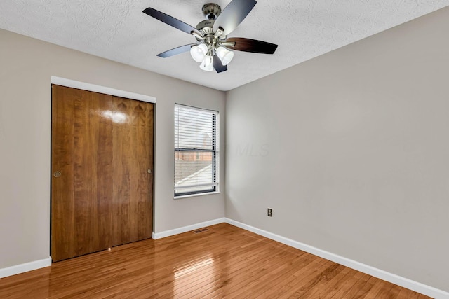 unfurnished bedroom featuring a textured ceiling, a closet, baseboards, and wood finished floors