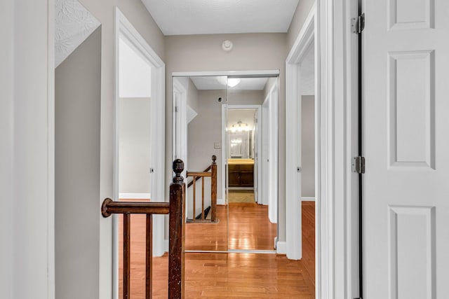 hall featuring a textured ceiling, light wood-type flooring, an upstairs landing, and baseboards