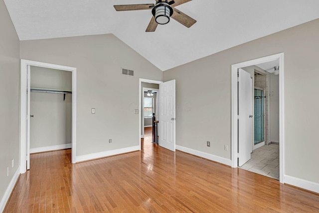 unfurnished bedroom with a walk in closet, visible vents, vaulted ceiling, and light wood-style flooring