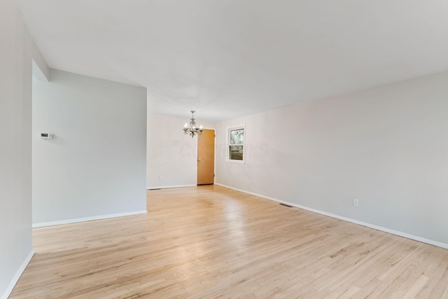 empty room featuring light wood-style floors, baseboards, and a chandelier