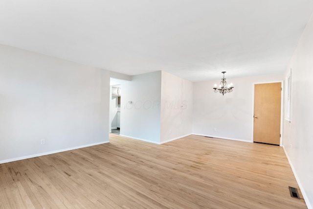 empty room featuring light wood-style floors, a chandelier, visible vents, and baseboards