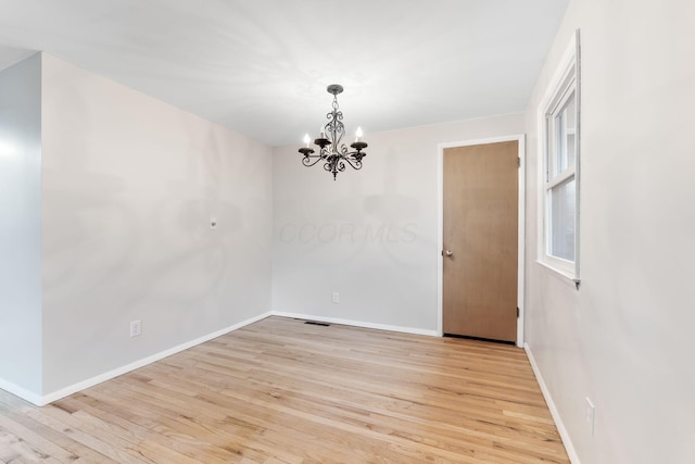 spare room featuring baseboards, an inviting chandelier, visible vents, and light wood-style floors