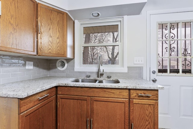 kitchen with light stone countertops, brown cabinetry, backsplash, and a sink