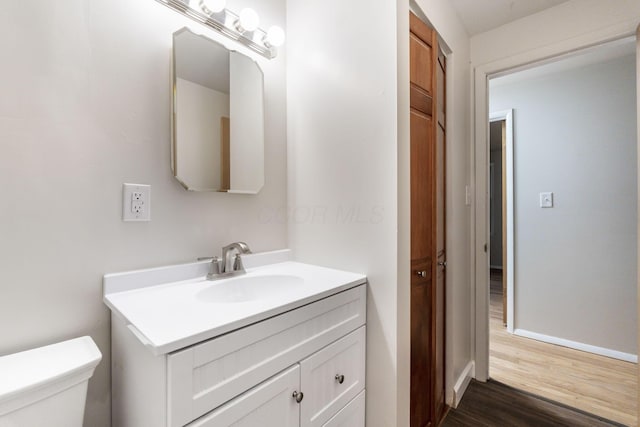 half bathroom featuring toilet, baseboards, wood finished floors, and vanity