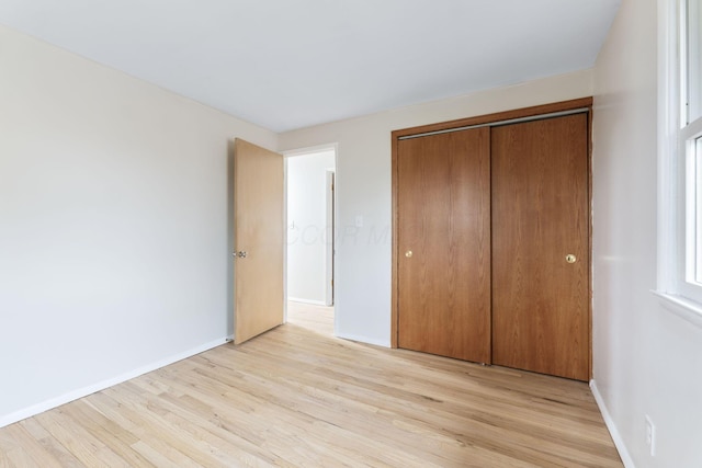 unfurnished bedroom featuring light wood-style floors, baseboards, and a closet