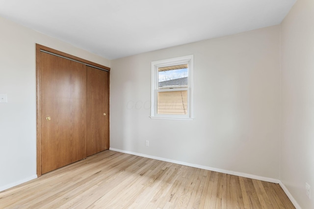 unfurnished bedroom featuring a closet, baseboards, and light wood finished floors