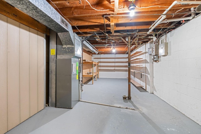 unfinished basement featuring concrete block wall, visible vents, and heating unit