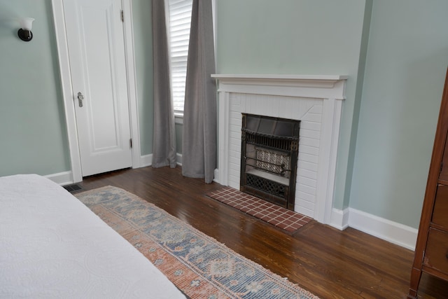 bedroom featuring a brick fireplace, visible vents, dark wood finished floors, and baseboards