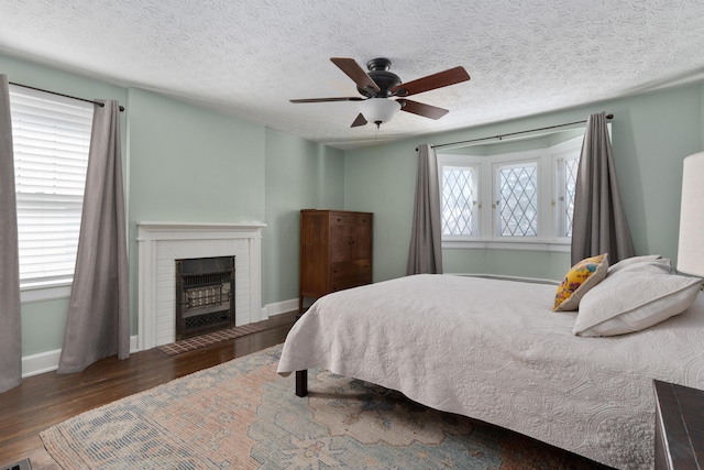 bedroom featuring a fireplace, baseboards, dark wood finished floors, and a ceiling fan