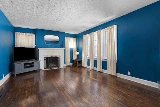 unfurnished living room with a textured ceiling, baseboards, dark wood-type flooring, and a stone fireplace