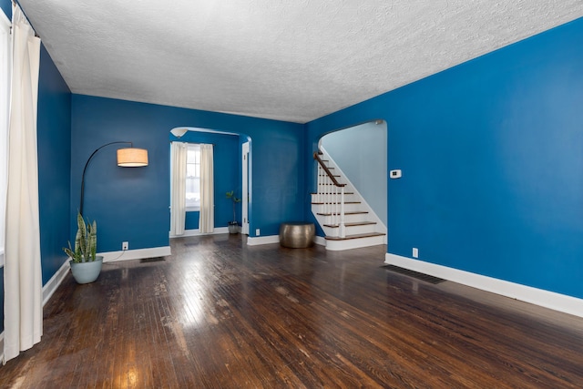 empty room featuring baseboards, arched walkways, wood finished floors, stairs, and a textured ceiling