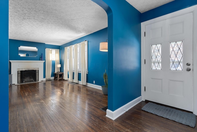 entryway with baseboards, a fireplace with raised hearth, arched walkways, dark wood finished floors, and a textured ceiling