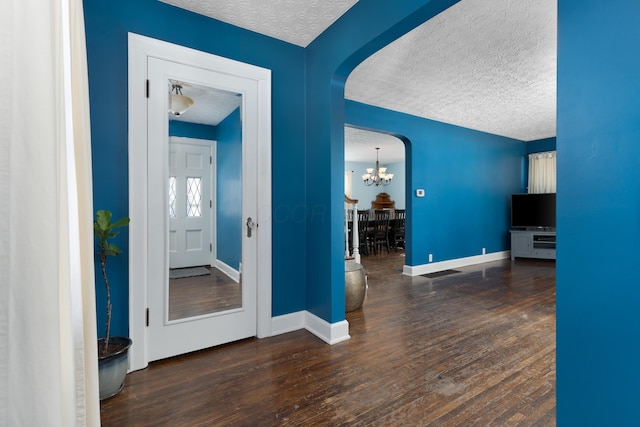 corridor with arched walkways, dark wood-style flooring, a textured ceiling, a chandelier, and baseboards