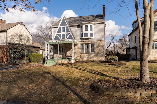 rear view of property with a porch, stone siding, a yard, and a chimney