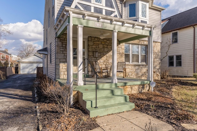 view of front of home featuring an outbuilding, stone siding, a porch, and a detached garage