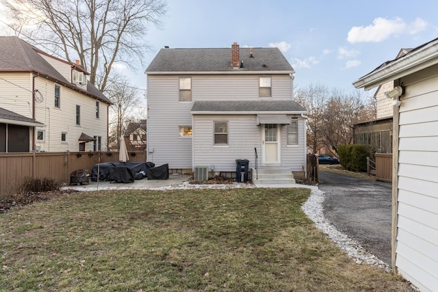 back of house featuring central air condition unit, a shingled roof, fence, a lawn, and a chimney