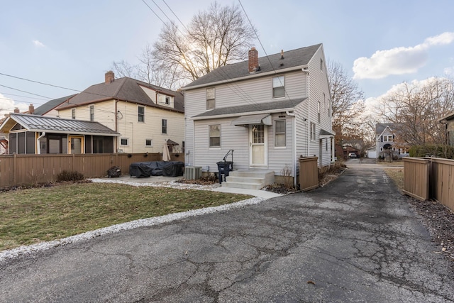 view of front of home featuring roof with shingles, central AC unit, a chimney, and a front yard