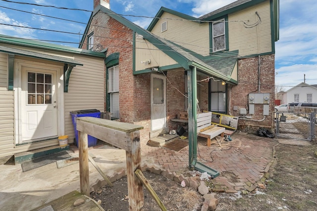 rear view of house with entry steps, brick siding, a chimney, and fence