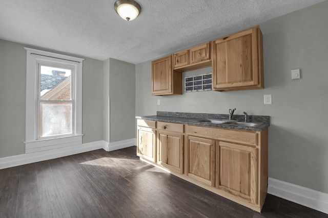 kitchen with a textured ceiling, dark wood-style flooring, a sink, baseboards, and dark countertops